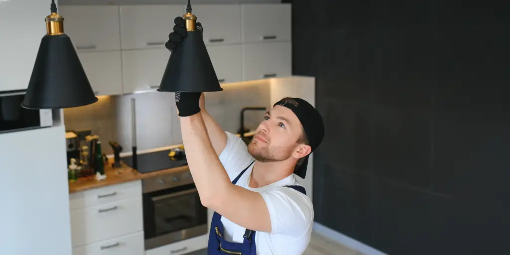 Mann in Arbeitskleidung richtet Lampe in moderner Küche aus.