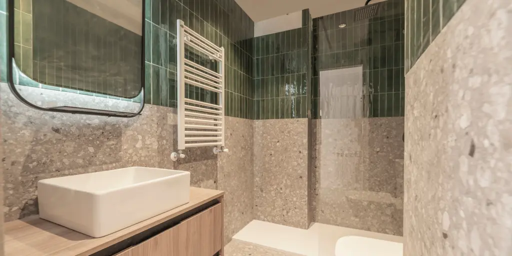 Modernes Bad mit grünem Fliesenspiegel, weißem Waschtisch, beigem Stein, Handtuchheizung und offener Dusche.