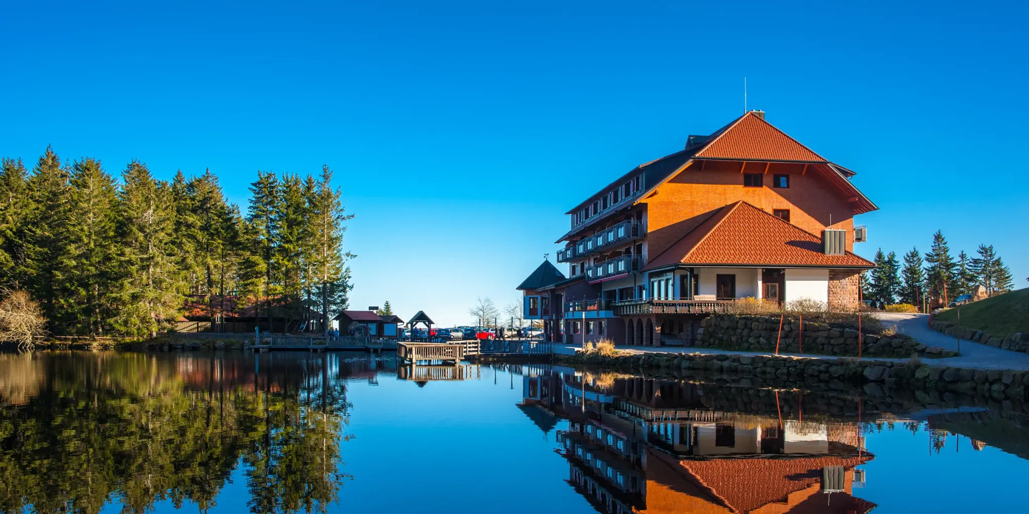 Hotel am Seeufer mit Wald und klarem Himmel, perfekte Spiegelung im Wasser.