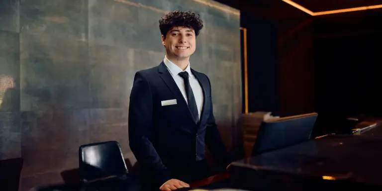 Ein lächelnder Mann im Anzug steht professionell hinter einem Empfangstresen.